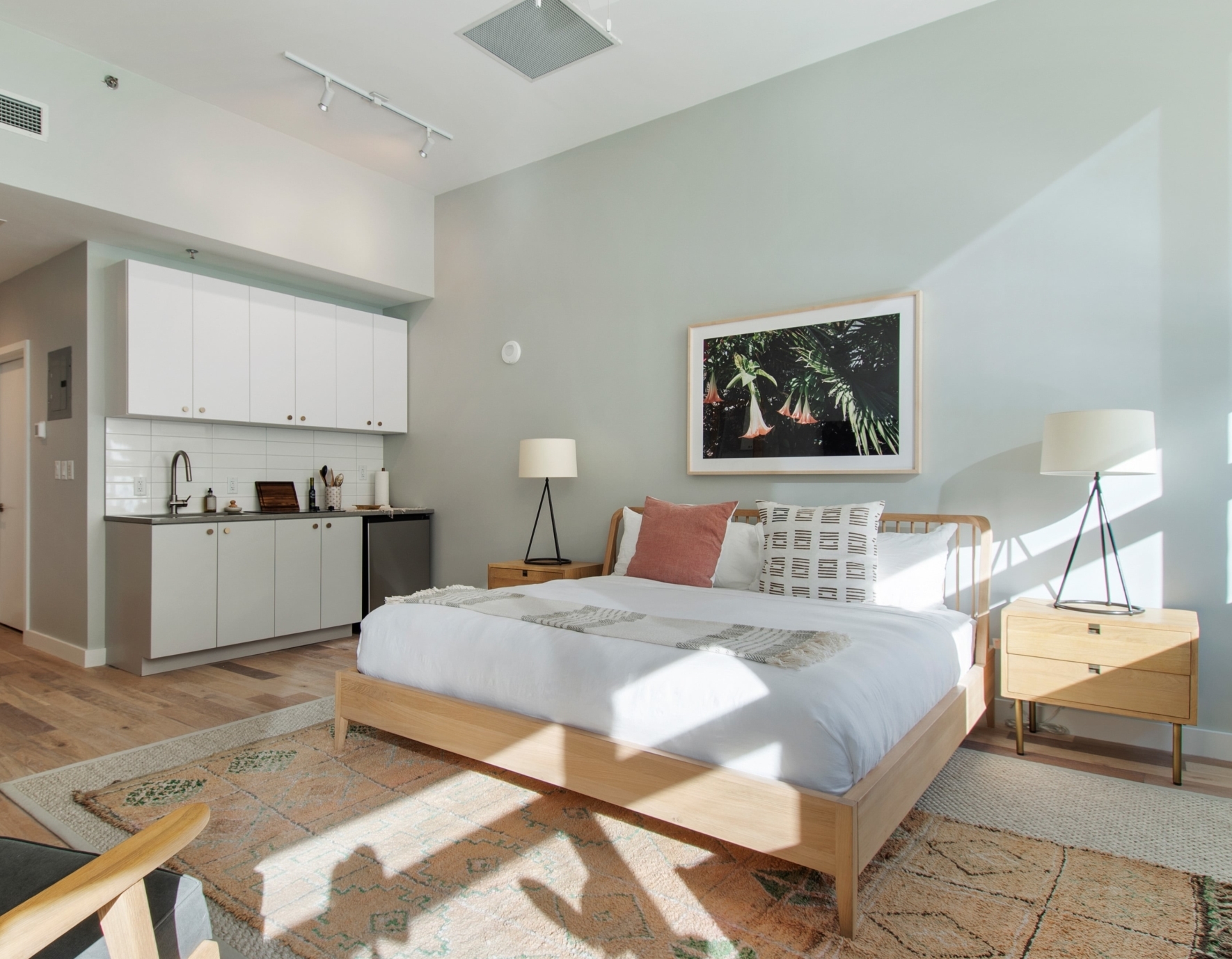 A studio guest suite with a simple kitchen and spacious bedroom space with ample natural light and modern furniture.